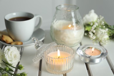 Photo of Beautiful burning candle, tea and flowers on white wooden table, closeup