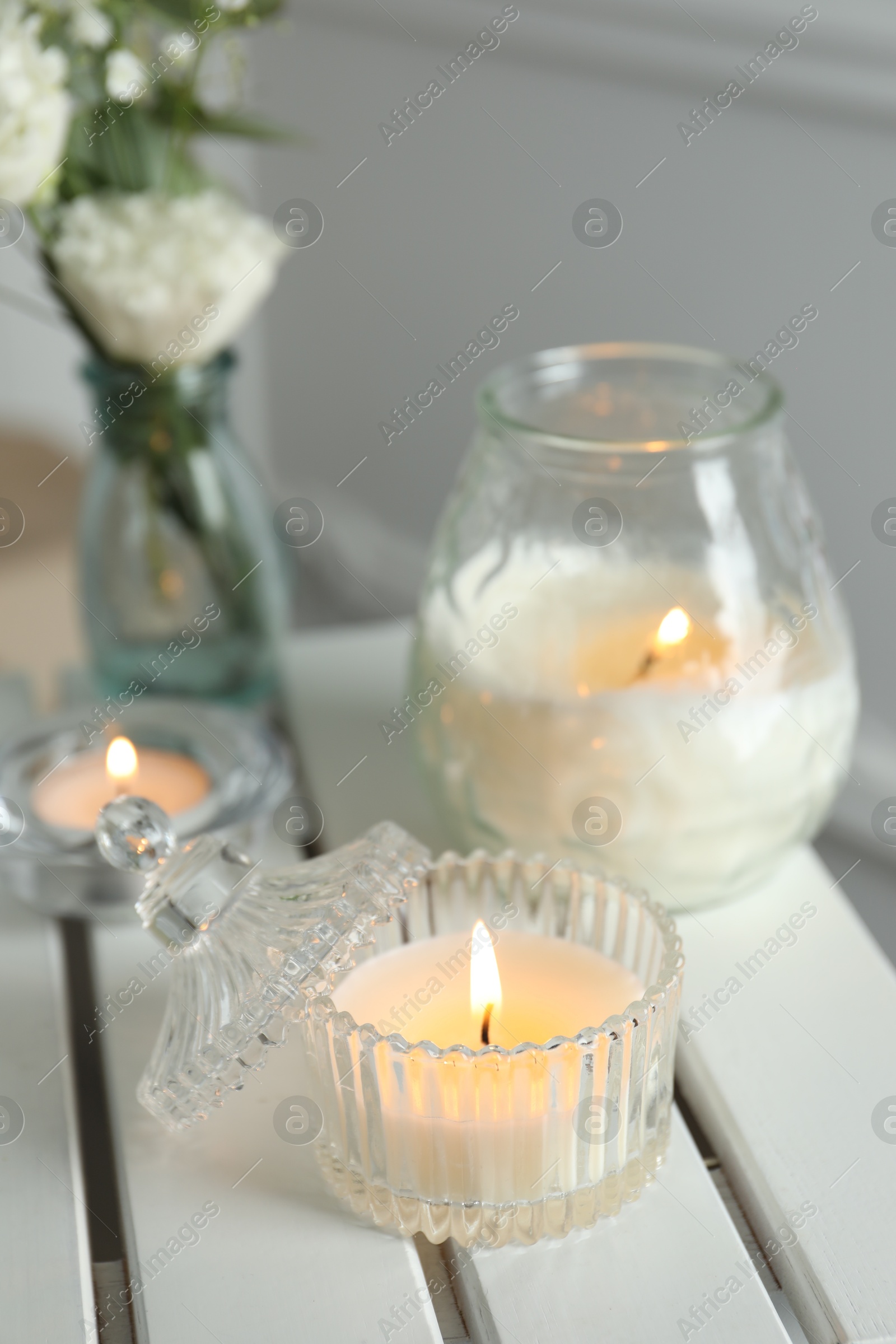 Photo of Beautiful burning candle and flowers on white wooden table, closeup