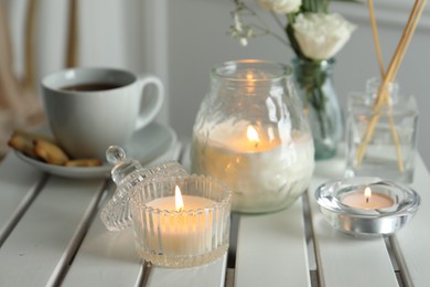 Photo of Beautiful burning candle and flowers on white wooden table, closeup