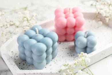 Photo of Beautiful bubble candles and flowers on white marble table, closeup