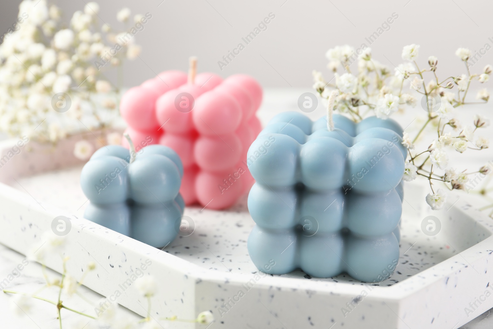 Photo of Beautiful bubble candles and flowers on white marble table, closeup