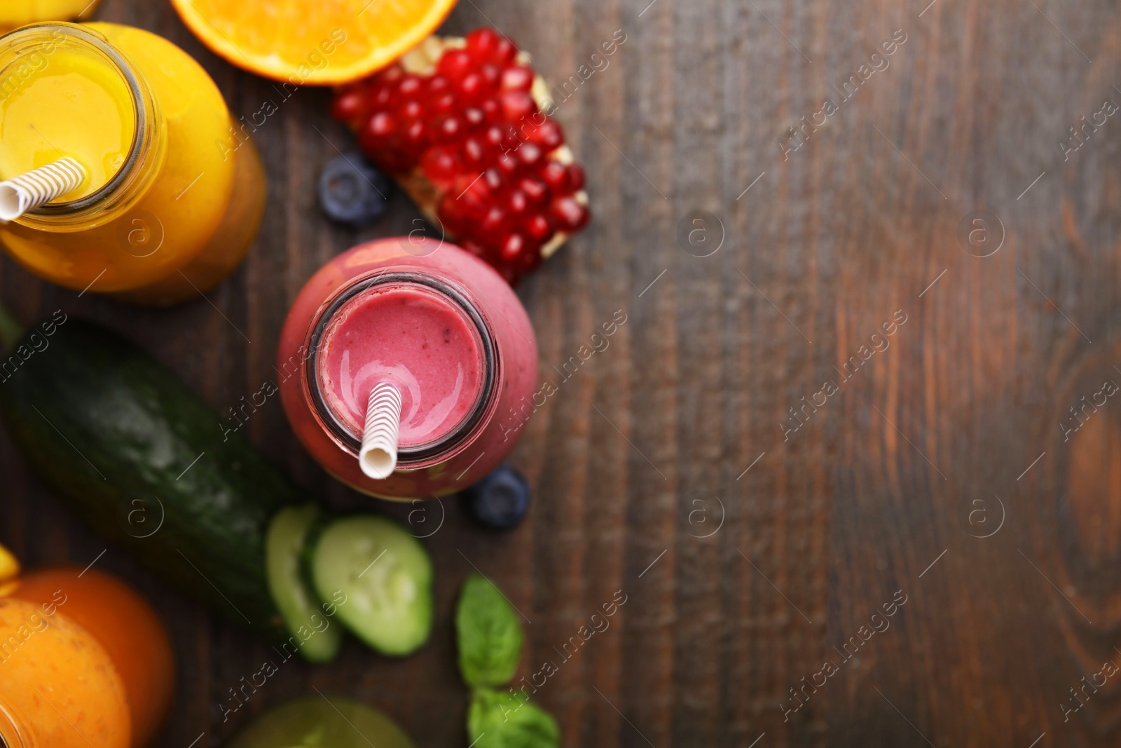 Photo of Glass bottles of tasty smoothies and different products on wooden table, flat lay. Space for text