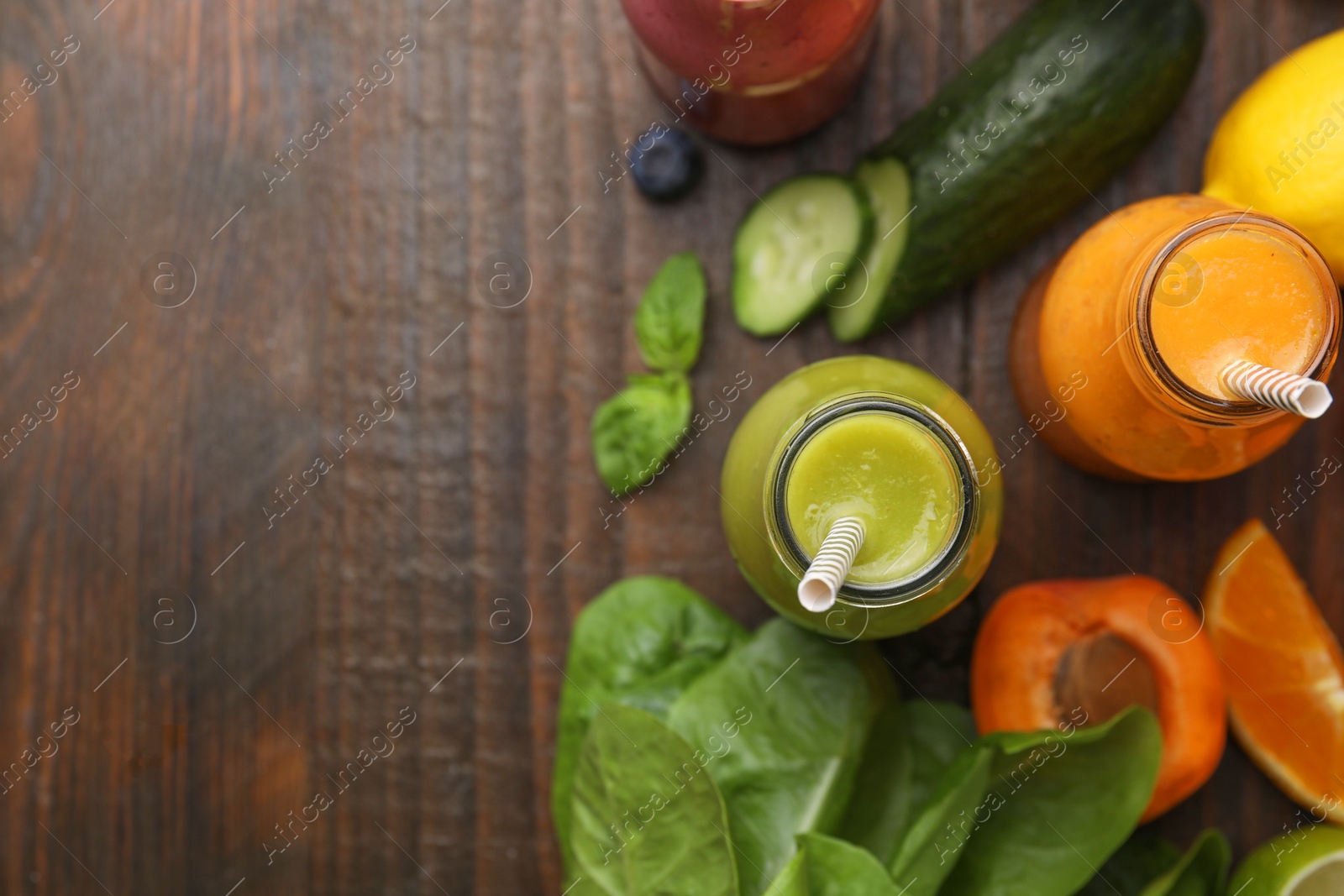 Photo of Glass bottles of tasty smoothies and different products on wooden table, flat lay. Space for text