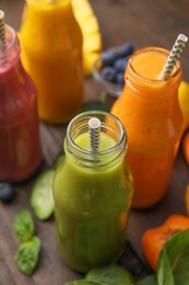 Photo of Glass bottles of tasty smoothies and different products on wooden table, closeup