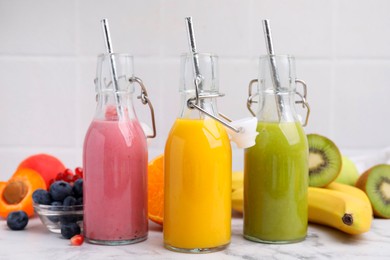 Glass bottles of tasty smoothies and different products on white marble table