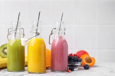 Glass bottles of tasty smoothies and different products on white marble table