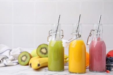 Glass bottles of tasty smoothies and different products on white marble table