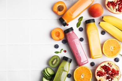 Photo of Glass bottles of tasty smoothies and different products on white tiled table, flat lay. Space for text