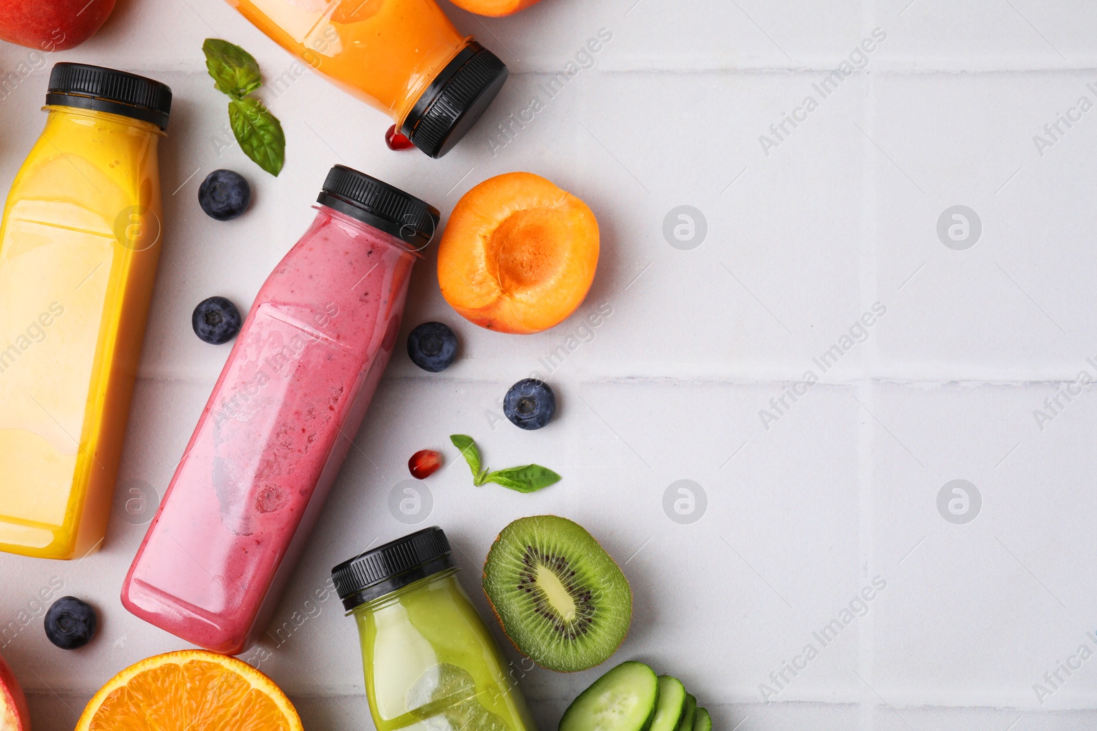 Photo of Glass bottles of tasty smoothies and different products on white tiled table, flat lay. Space for text