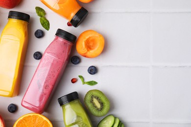 Glass bottles of tasty smoothies and different products on white tiled table, flat lay. Space for text