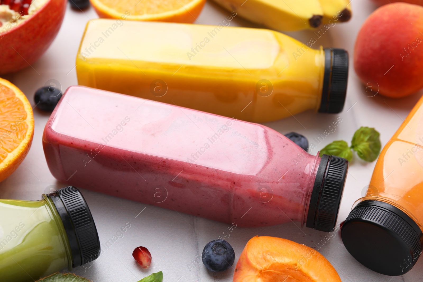 Photo of Glass bottles of tasty smoothies and different products on white tiled table, closeup