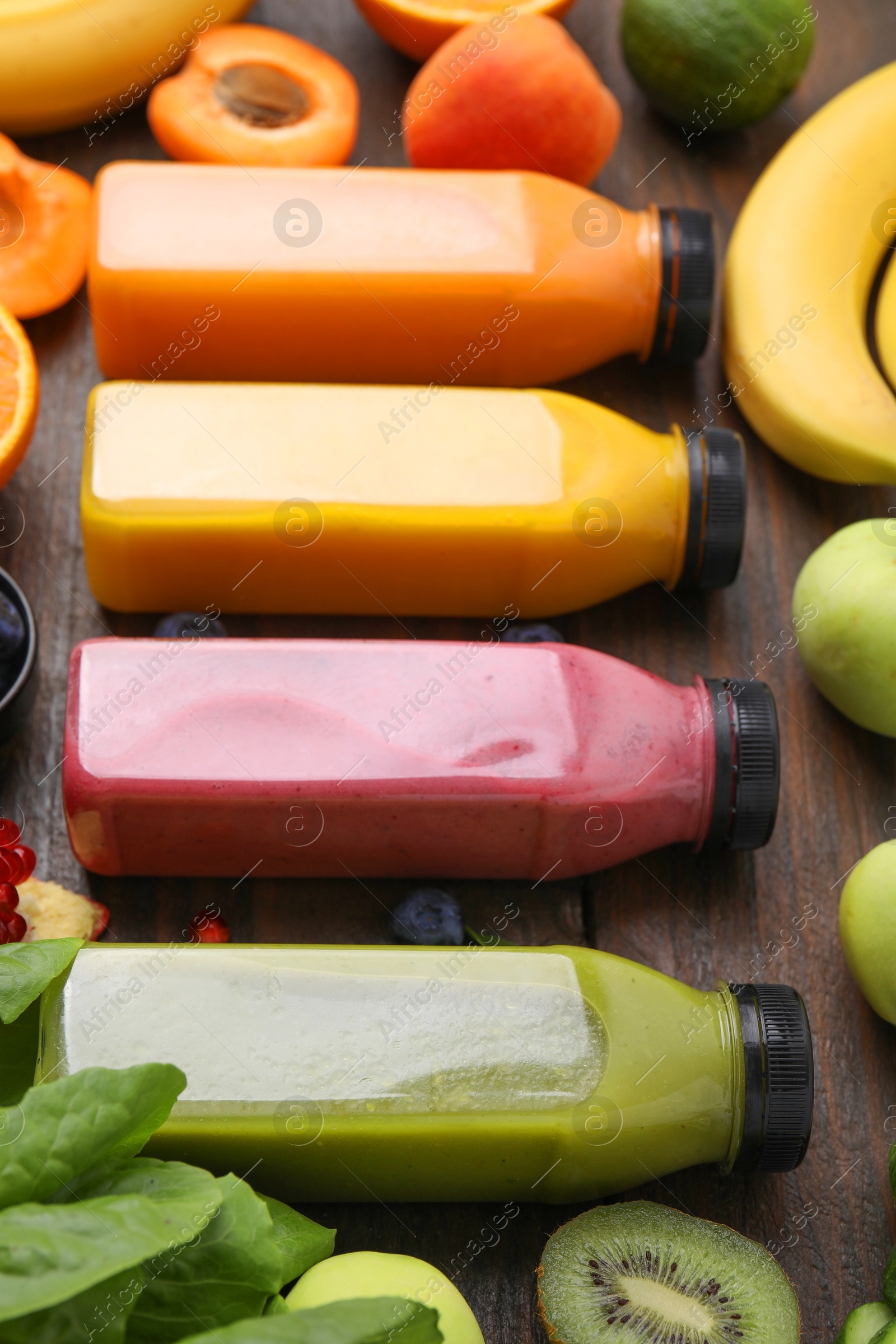 Photo of Glass bottles of tasty smoothies and different products on wooden table