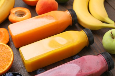 Glass bottles of tasty smoothies and different products on wooden table, closeup