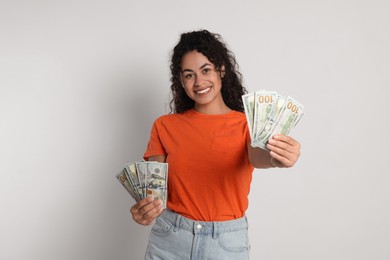 Happy woman with dollar banknotes on light grey background