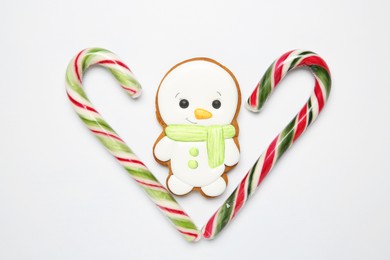 Photo of Delicious cookie in shape of snowman and candy canes on white background, flat lay. Christmas sweets