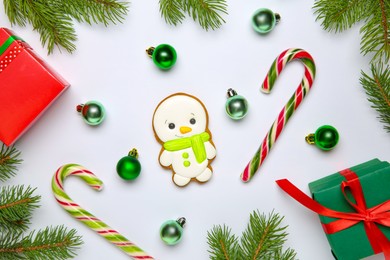 Photo of Delicious cookie in shape of snowman, candy canes, gift boxes, Christmas balls and fir tree branches on white background, flat lay