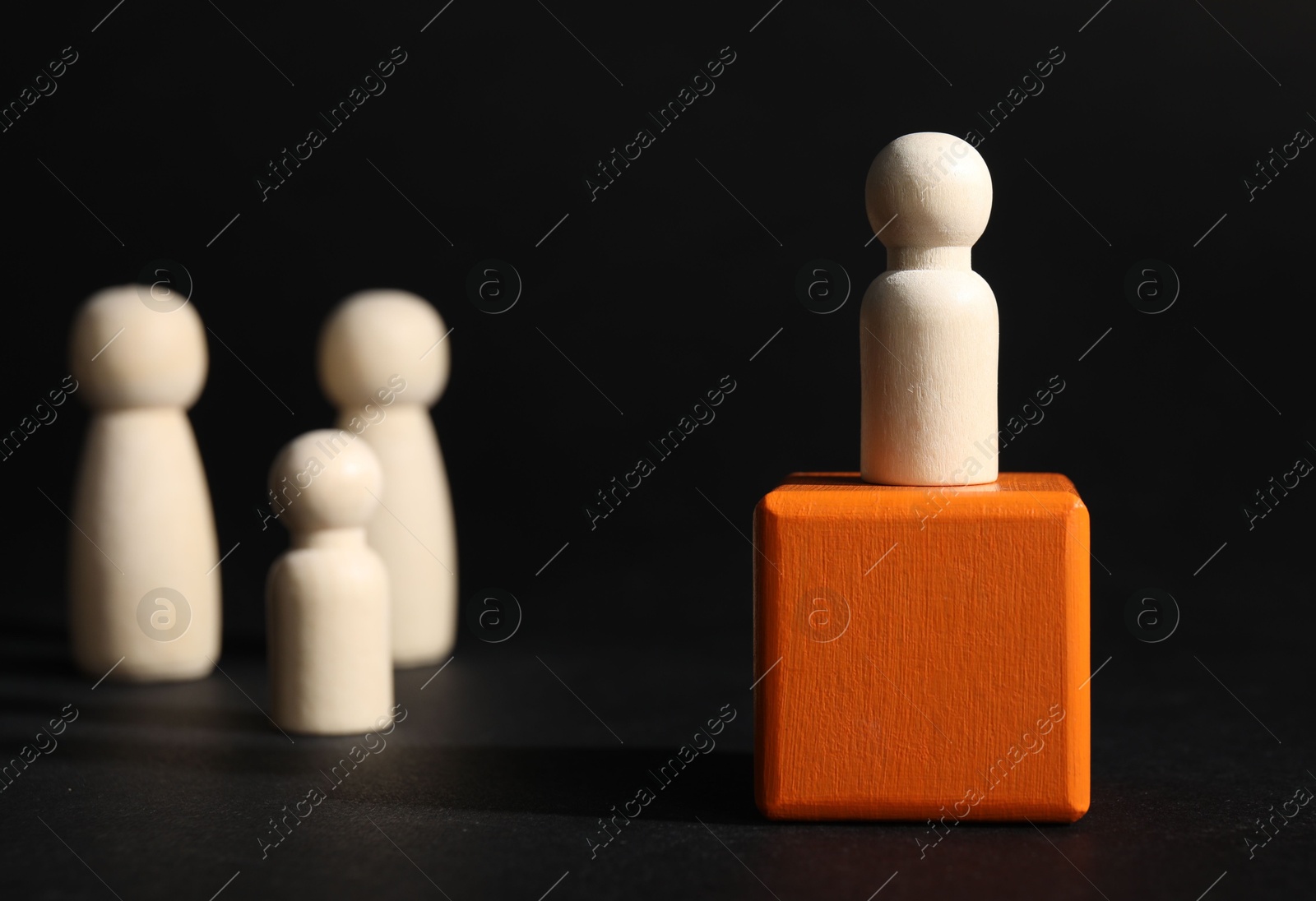 Photo of Winner concept. One wooden figure on cube among others against black background, selective focus