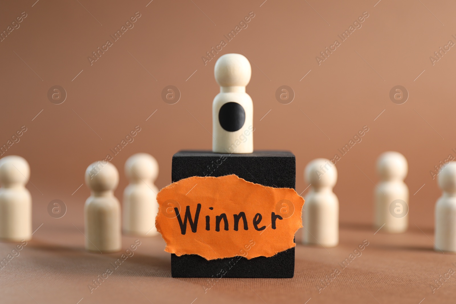 Photo of Winner concept. One wooden figure on cube among others against light brown background, selective focus