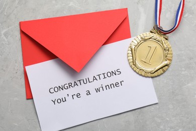 Photo of Card with phrase Congratulations You`re Winner, envelope and golden medal on grey marble table, flat lay