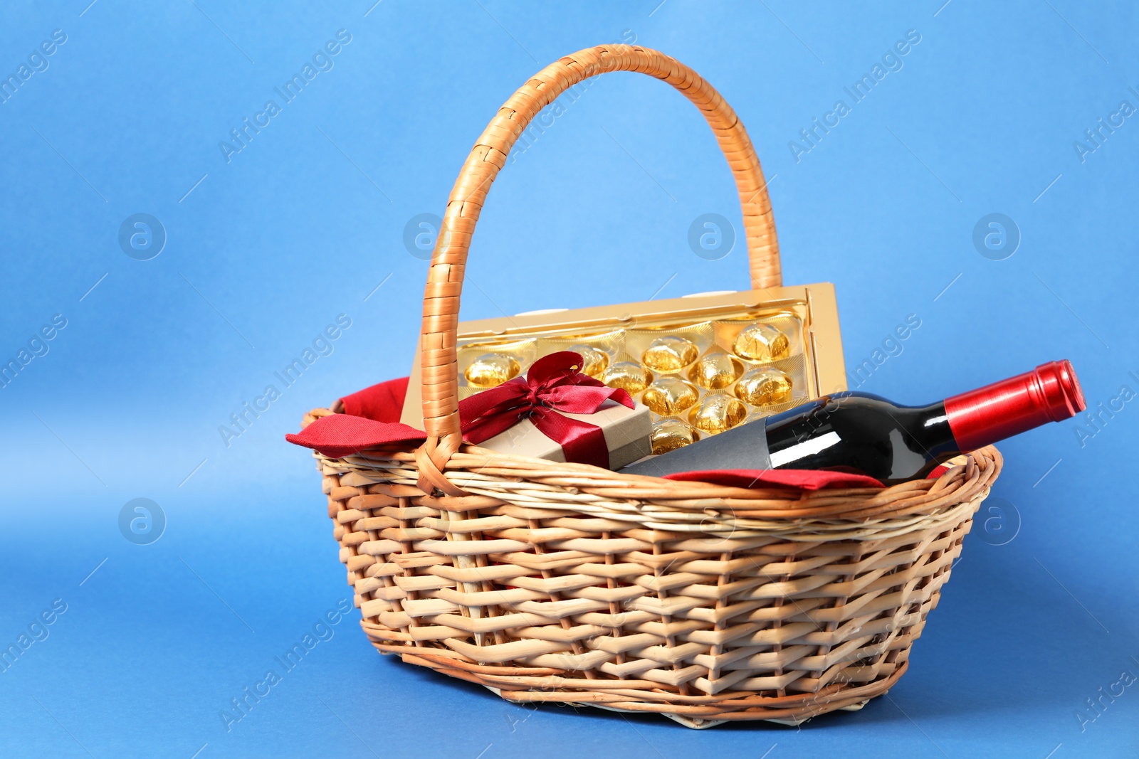 Photo of Wicker gift basket with wine on blue background