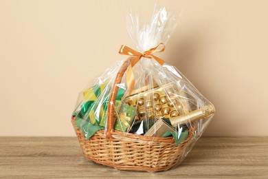 Photo of Wicker gift basket on wooden table against beige background