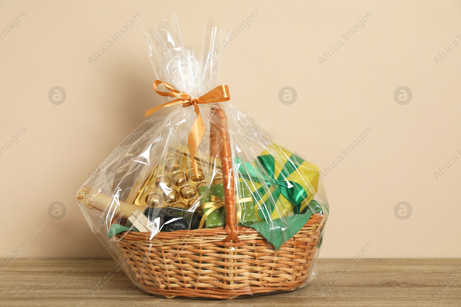 Photo of Wicker gift basket on wooden table against beige background