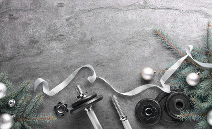 Photo of Barbell, dumbbell parts and Christmas decor on grey background, flat lay. Space for text