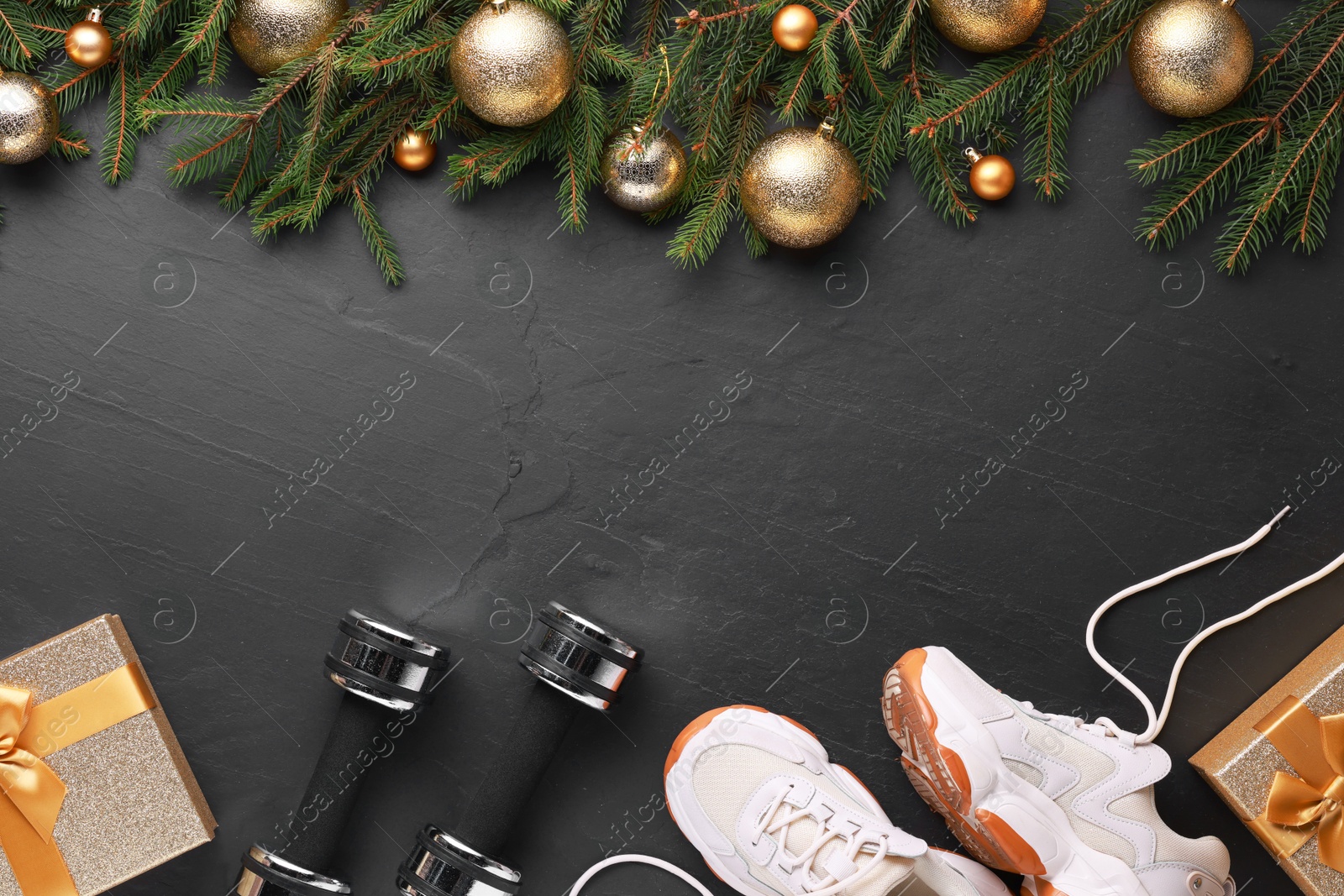 Photo of Dumbbells, gift boxes, sneakers and Christmas decor on black background, flat lay. Space for text