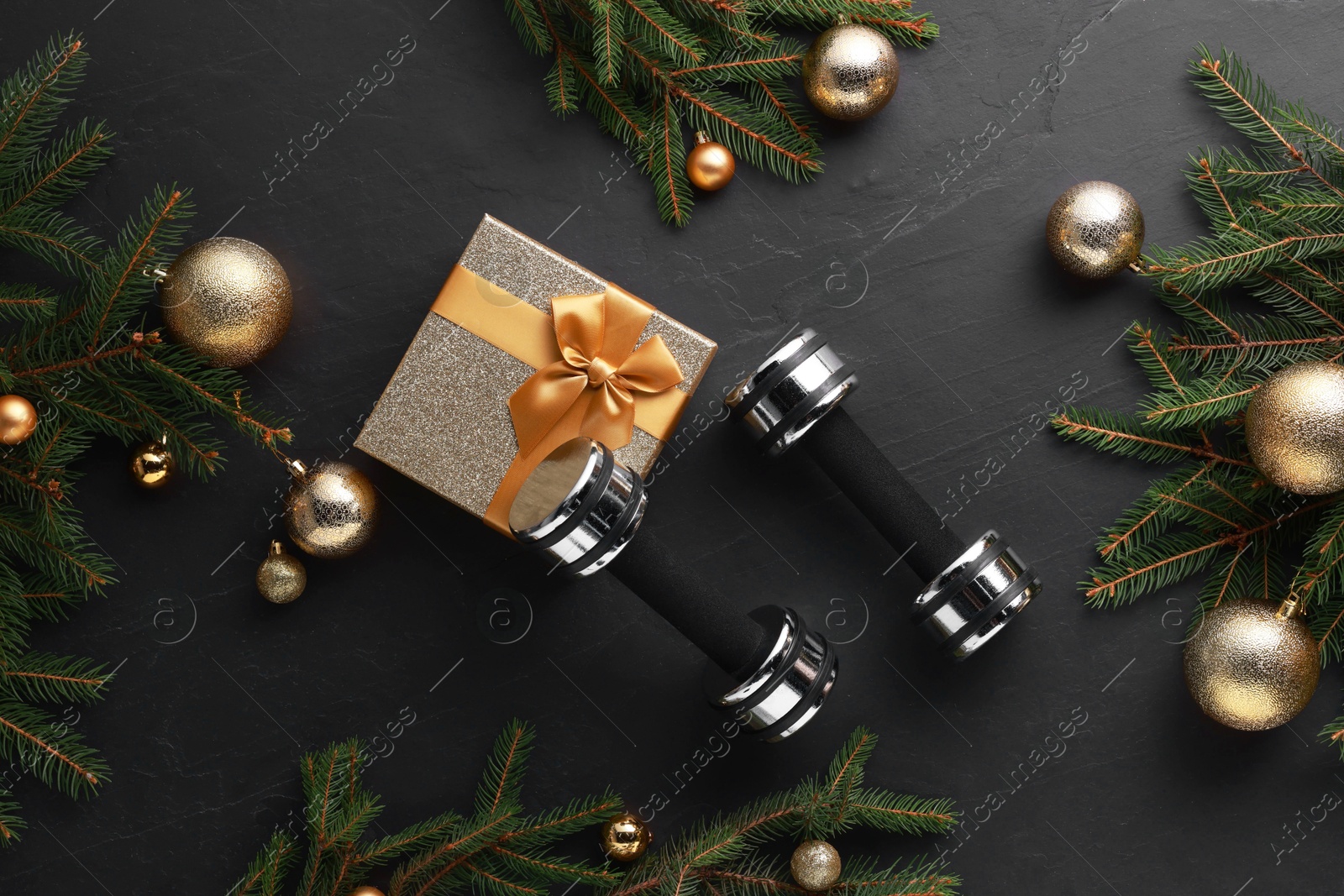 Photo of Dumbbells, gift box and Christmas decor on black background, flat lay