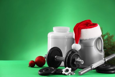 Photo of Dumbbells, containers with supplements and Christmas decor on green background. Space for text