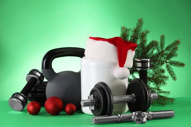 Photo of Dumbbells, kettlebell, container with supplement and Christmas decor on green background