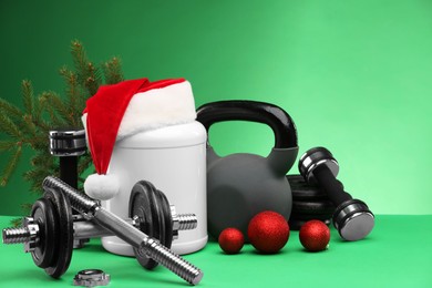 Photo of Dumbbells, kettlebell, container with supplement and Christmas decor on green background