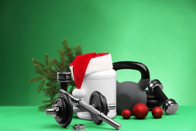 Photo of Dumbbells, kettlebell, container with supplement and Christmas decor on green background. Space for text