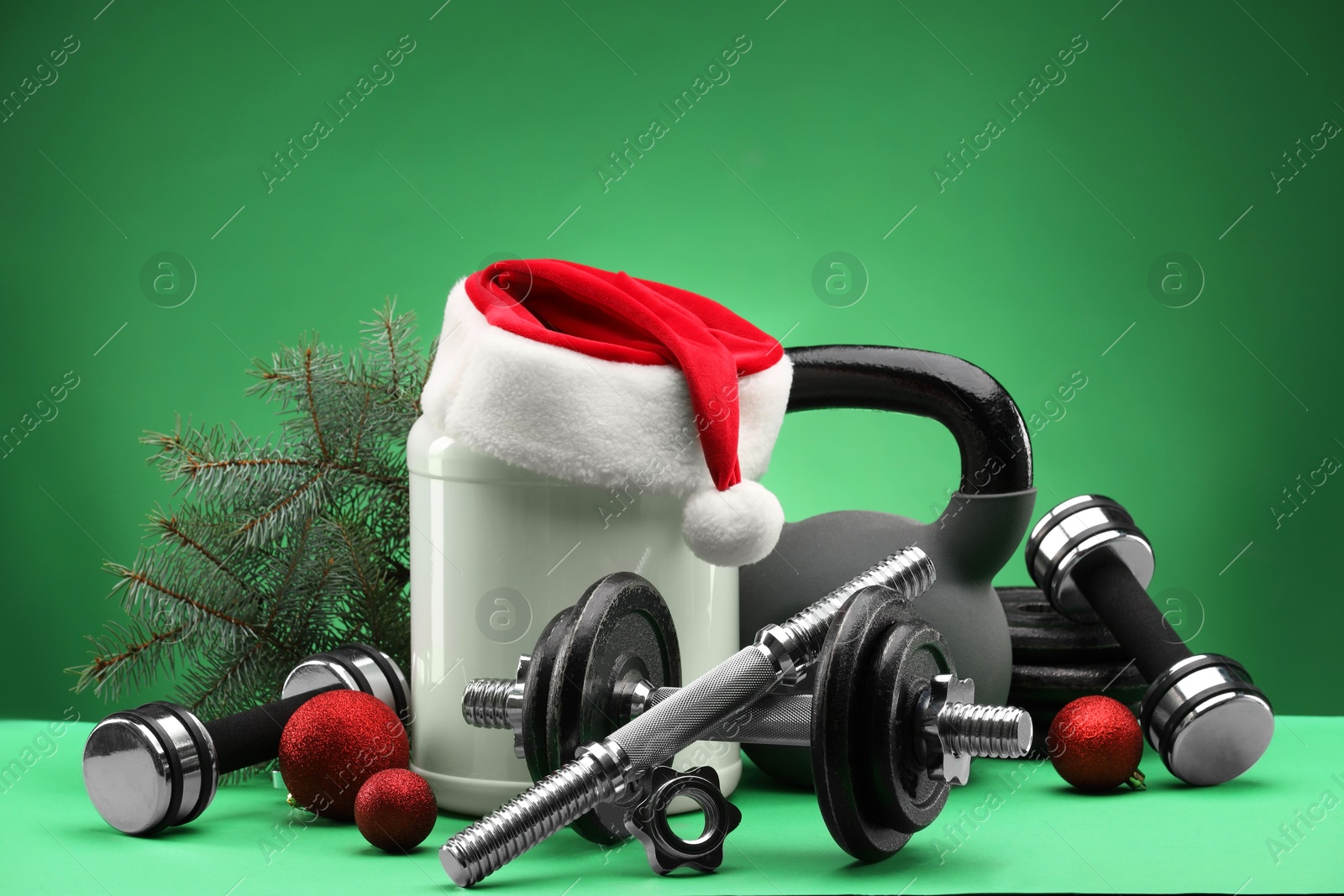 Photo of Dumbbells, kettlebell, container with supplement and Christmas decor on green background