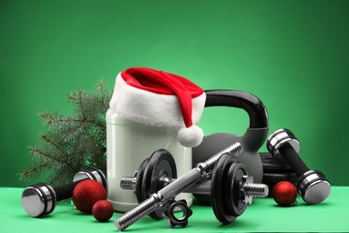 Photo of Dumbbells, kettlebell, container with supplement and Christmas decor on green background