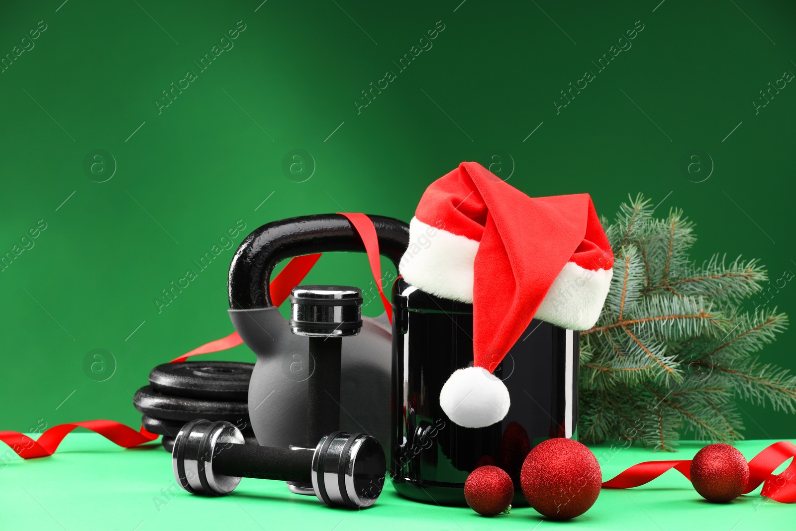 Photo of Dumbbells, kettlebell, container with supplement and Christmas decor on green background. Space for text