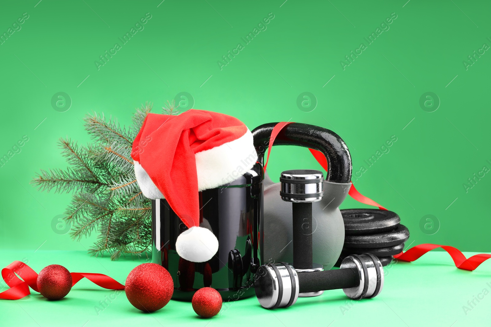 Photo of Dumbbells, kettlebell, container with supplement and Christmas decor on green background