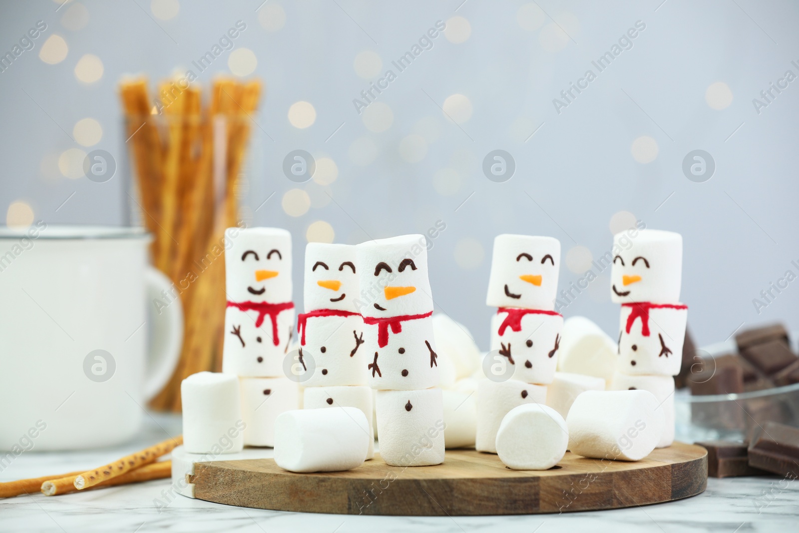 Photo of Funny snowmen made with marshmallows and other treats on white table against blurred lights