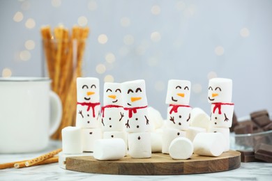 Photo of Funny snowmen made with marshmallows and other treats on white table against blurred lights