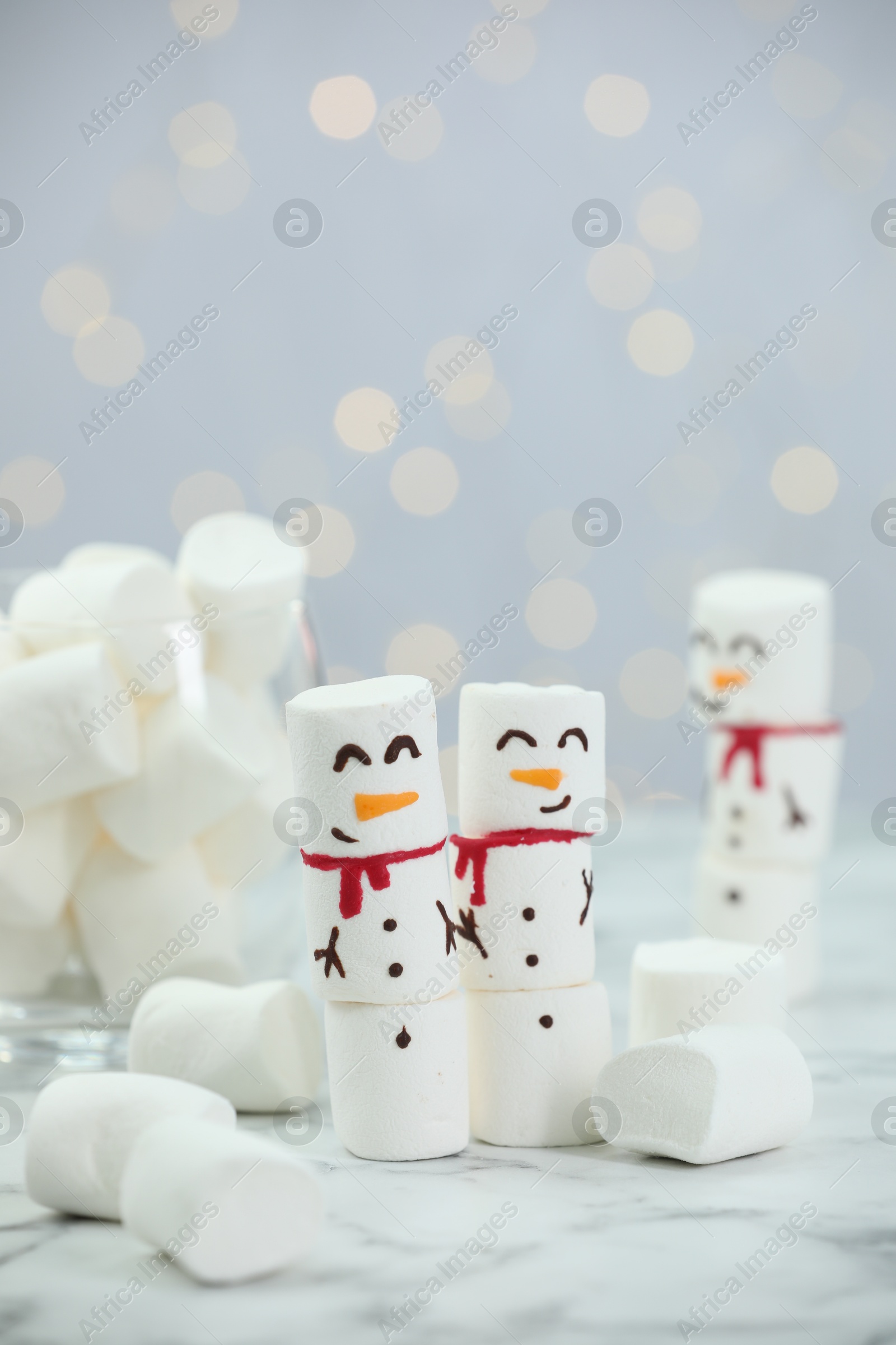 Photo of Funny snowmen made with marshmallows on white table against blurred lights