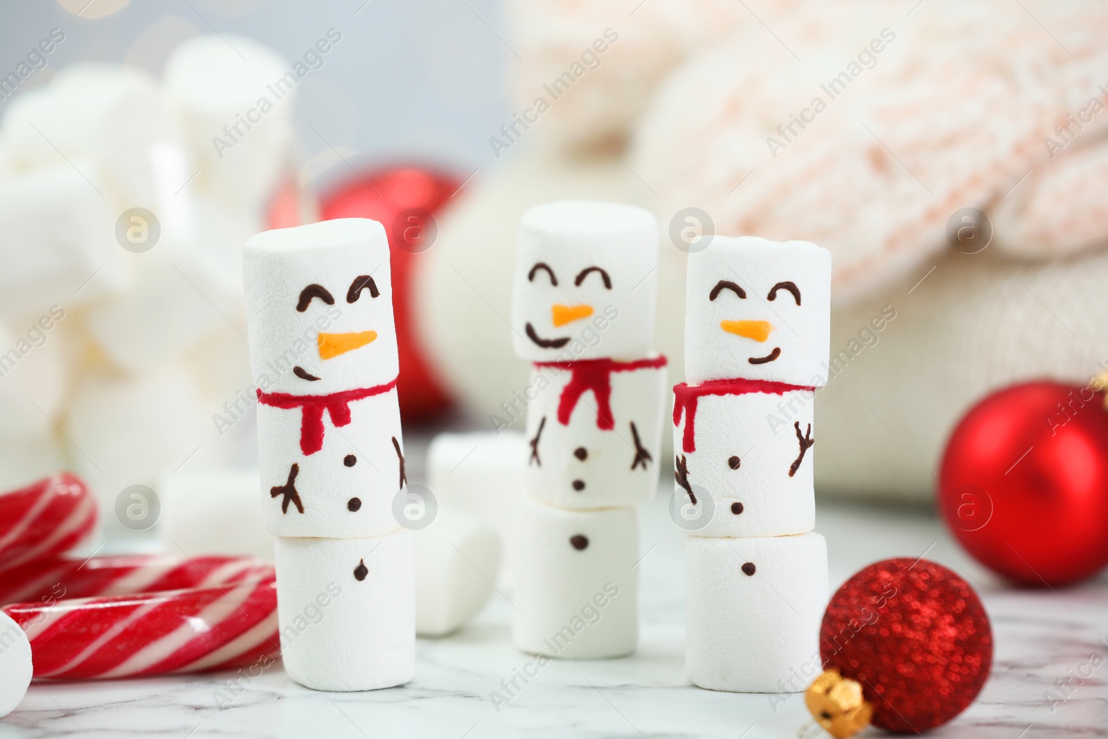 Photo of Funny snowmen made with marshmallows and Christmas decor on white table, closeup