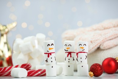 Funny snowmen made with marshmallows and Christmas decor on white table against blurred lights