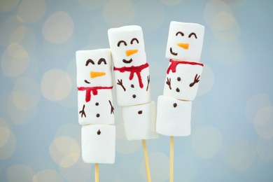 Photo of Funny snowmen made of marshmallows on light background with blurred lights