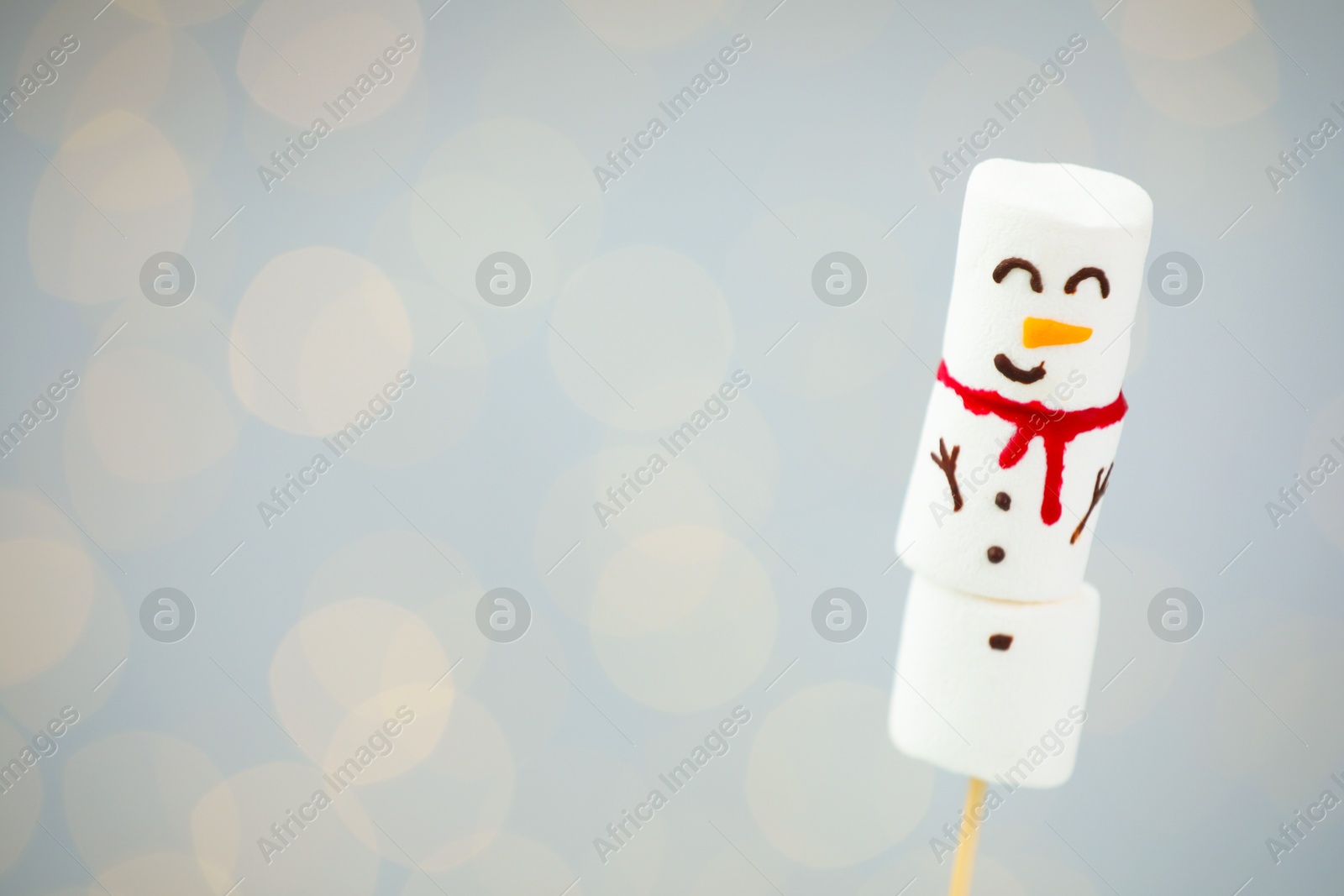 Photo of Funny snowman made of marshmallows on light background with blurred lights. Space for text