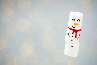 Photo of Funny snowman made of marshmallows on light background with blurred lights. Space for text