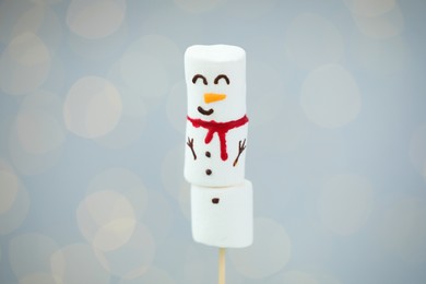 Funny snowman made of marshmallows on light background with blurred lights