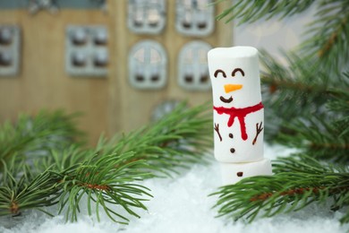 Photo of Funny snowman made with marshmallows and fir tree branches on artificial snow, closeup