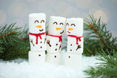 Photo of Funny snowmen made with marshmallows and fir tree branches on artificial snow against blurred lights, closeup