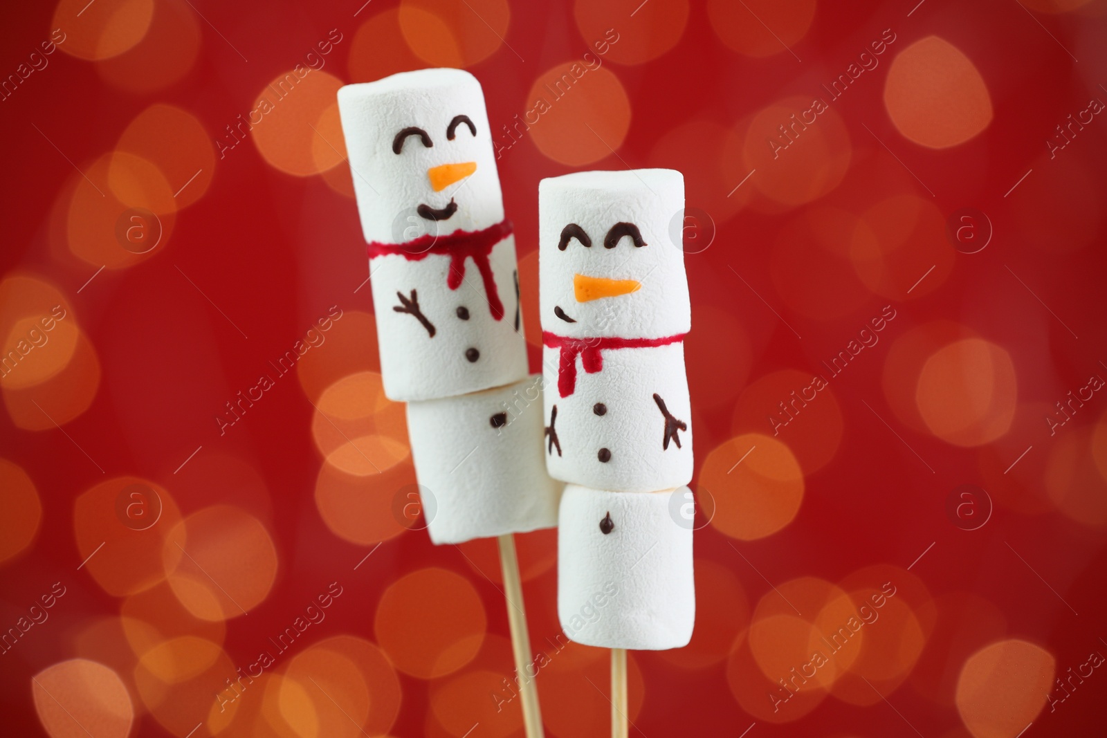 Photo of Funny snowmen made of marshmallows on red background with blurred lights