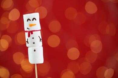 Photo of Funny snowman made of marshmallows on red background with blurred lights. Space for text